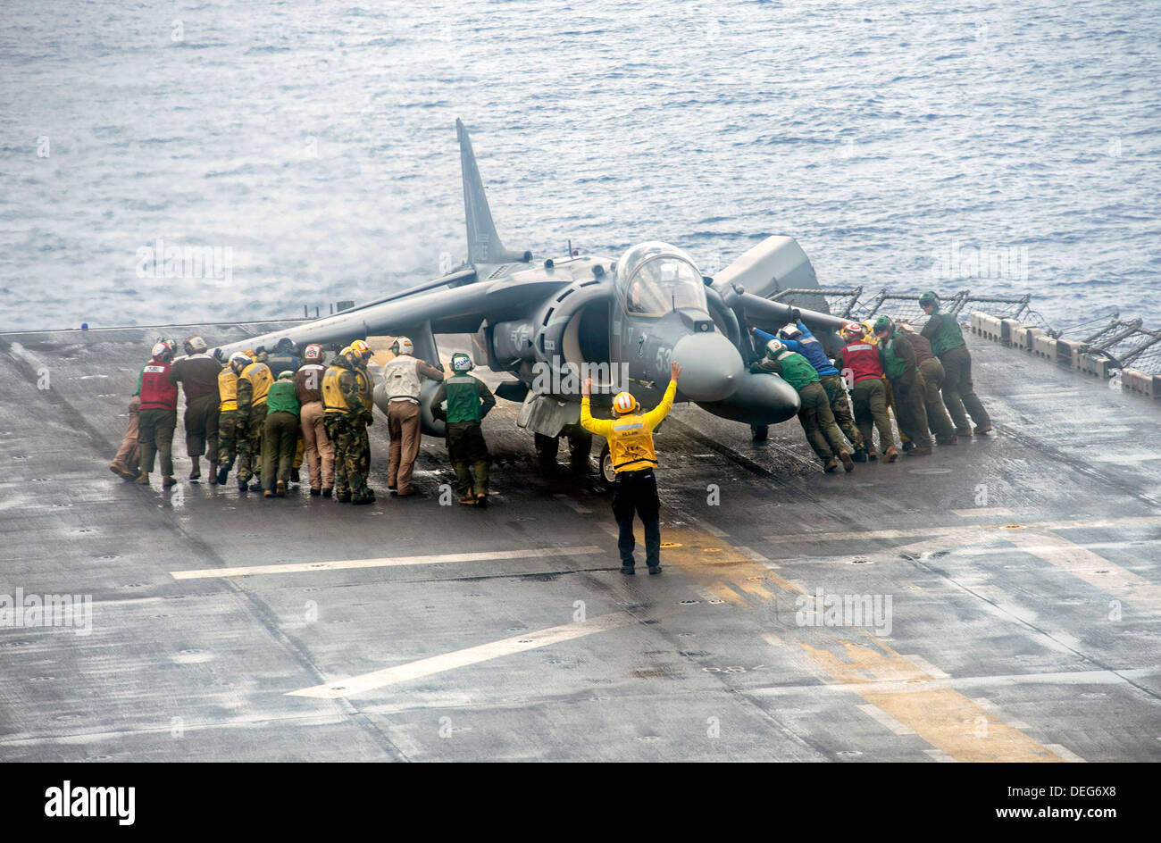 US Sailors and Marines move a Marine Corps AV-8B Harrier II aircraft during a rain storm on the flight deck of the amphibious assault ship USS Boxer September 11, 2013 underway in the Pacific Ocean Sept. 11, 2013. The Boxer was underway in the U.S. 7th Fleet area of responsibility supporting maritime security operations and theater security cooperation efforts. Stock Photo