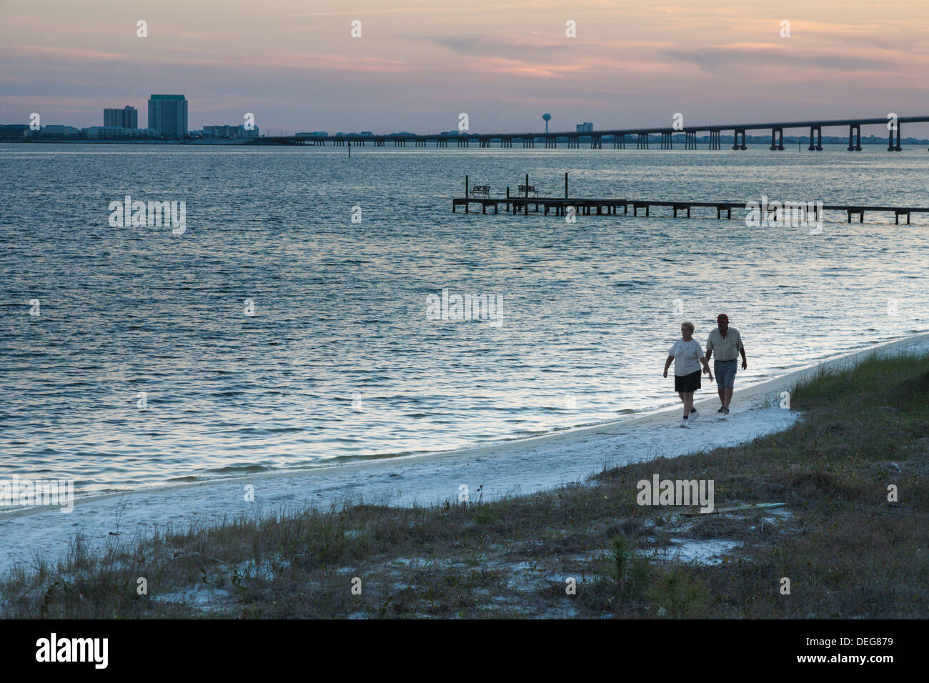 Senior couple walk on the white sand beach of Santa Rosa Sound at dusk in Navarre, Florida Stock Photo