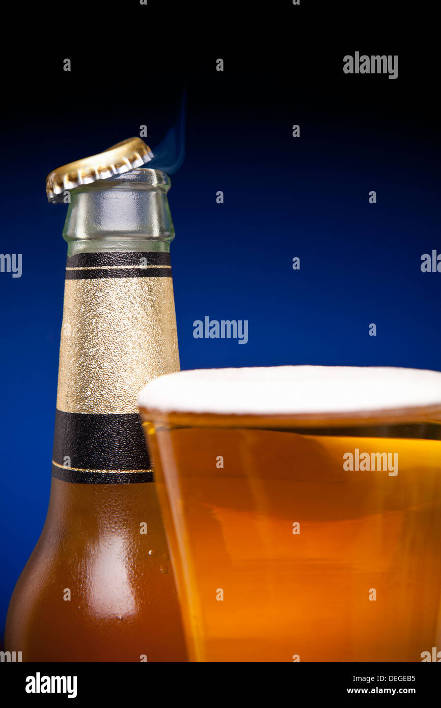 A cap is flying away from a beer bottle and a full glass. Stock Photo