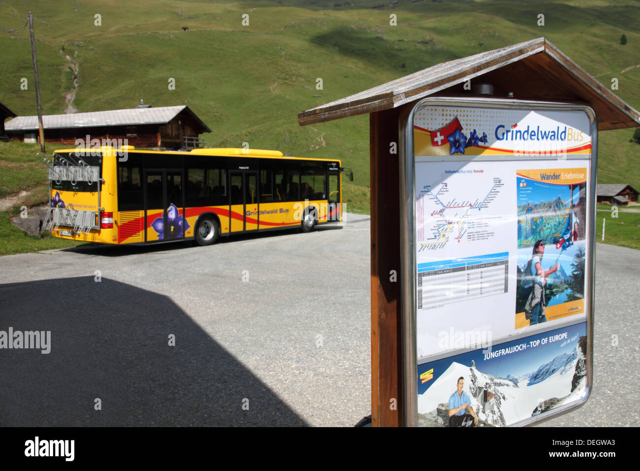 Yellow Swiss postbus parked by a bus stop sign. Stock Photo
