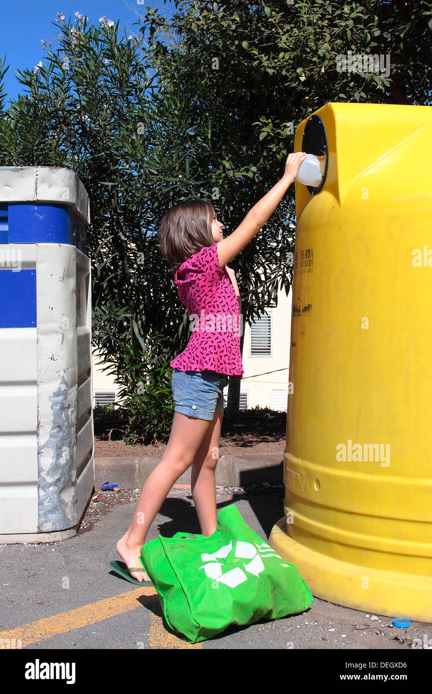 a young girl (7-8 years) stretching to put a plastic bottle in the recycling container. Stock Photo
