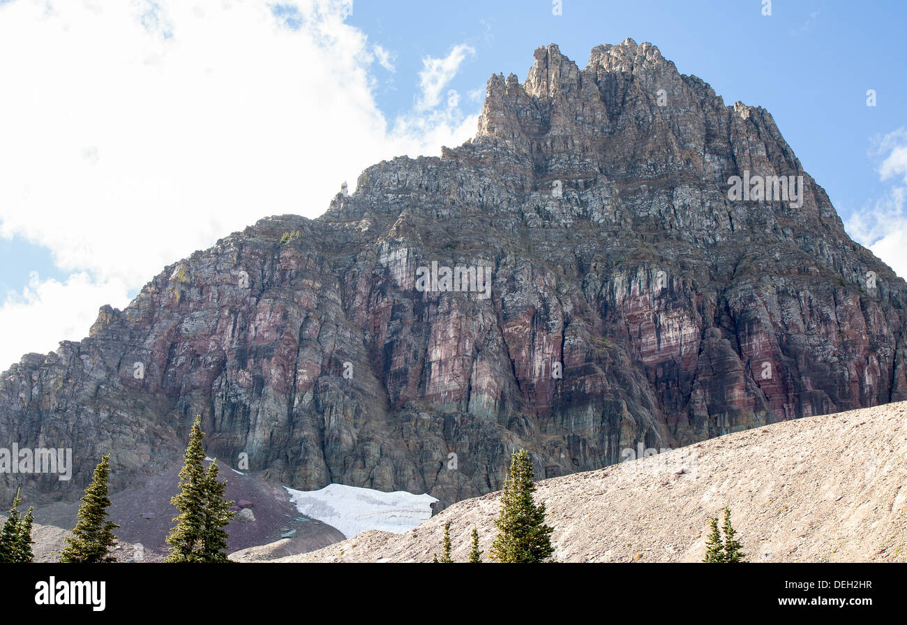 This image of Mount Reynolds at Glacier National Park shows purple rock face and remnants of a snow field. Stock Photo