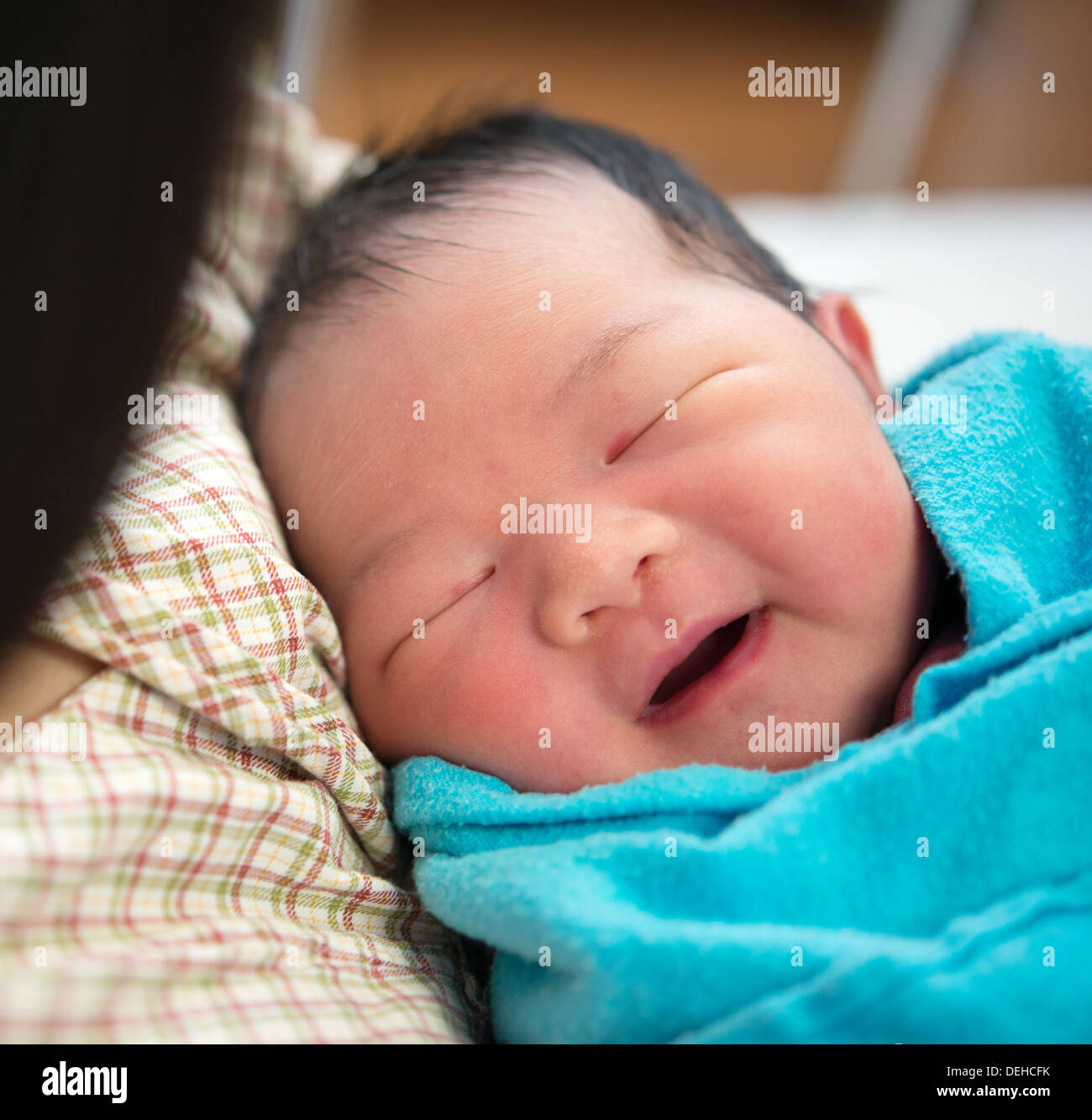 Newborn Asian baby girl smiling and fall asleep in mother's arms, inside hospital room Stock Photo