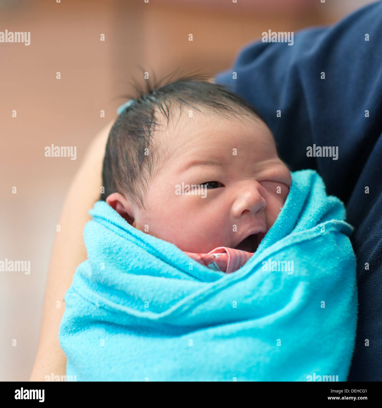 Newborn Asian baby girl smiling in father's arms, inside hospital room Stock Photo