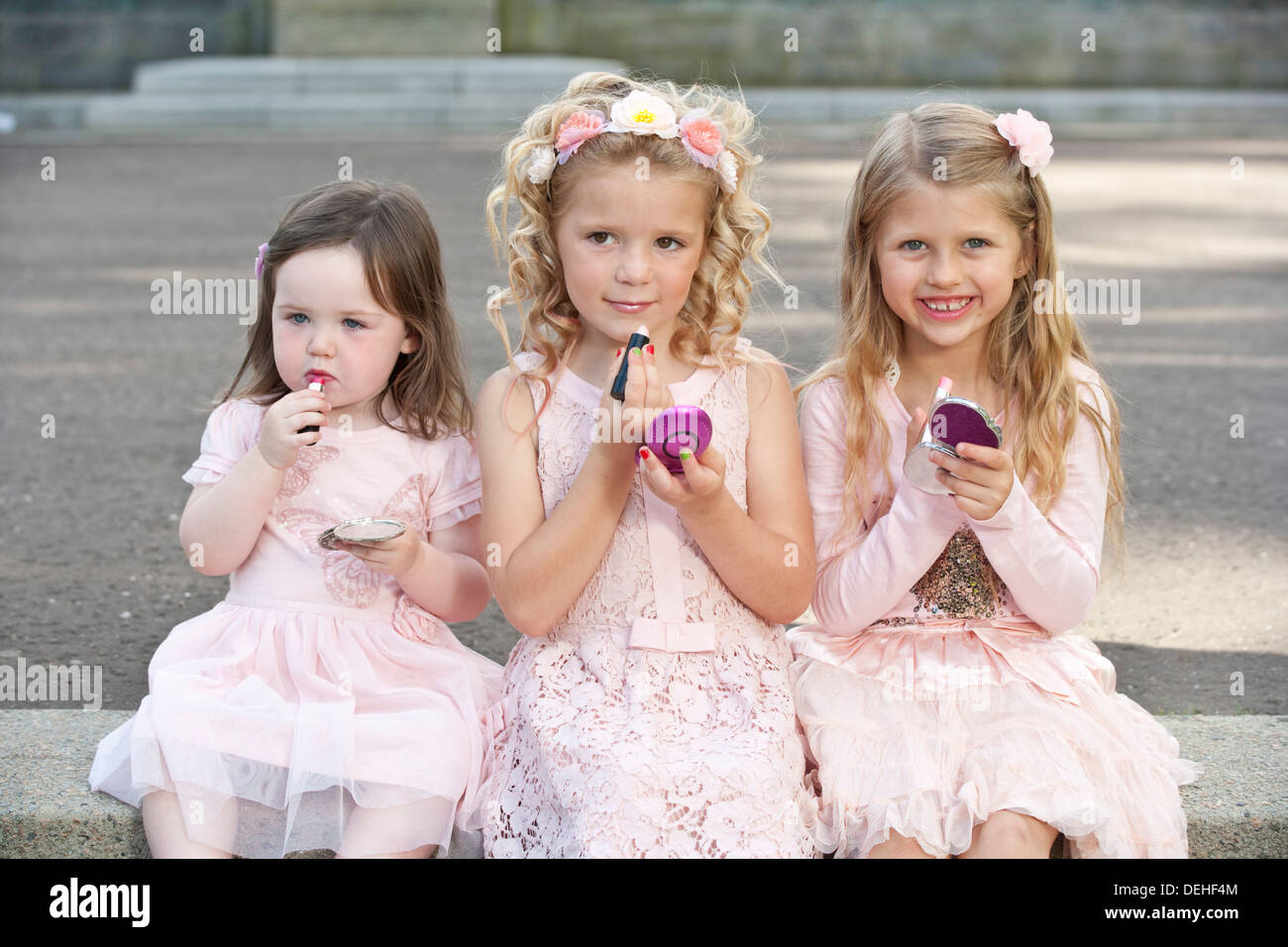 Three young preteen girls wearing pink dresses and applying make up. Stock Photo