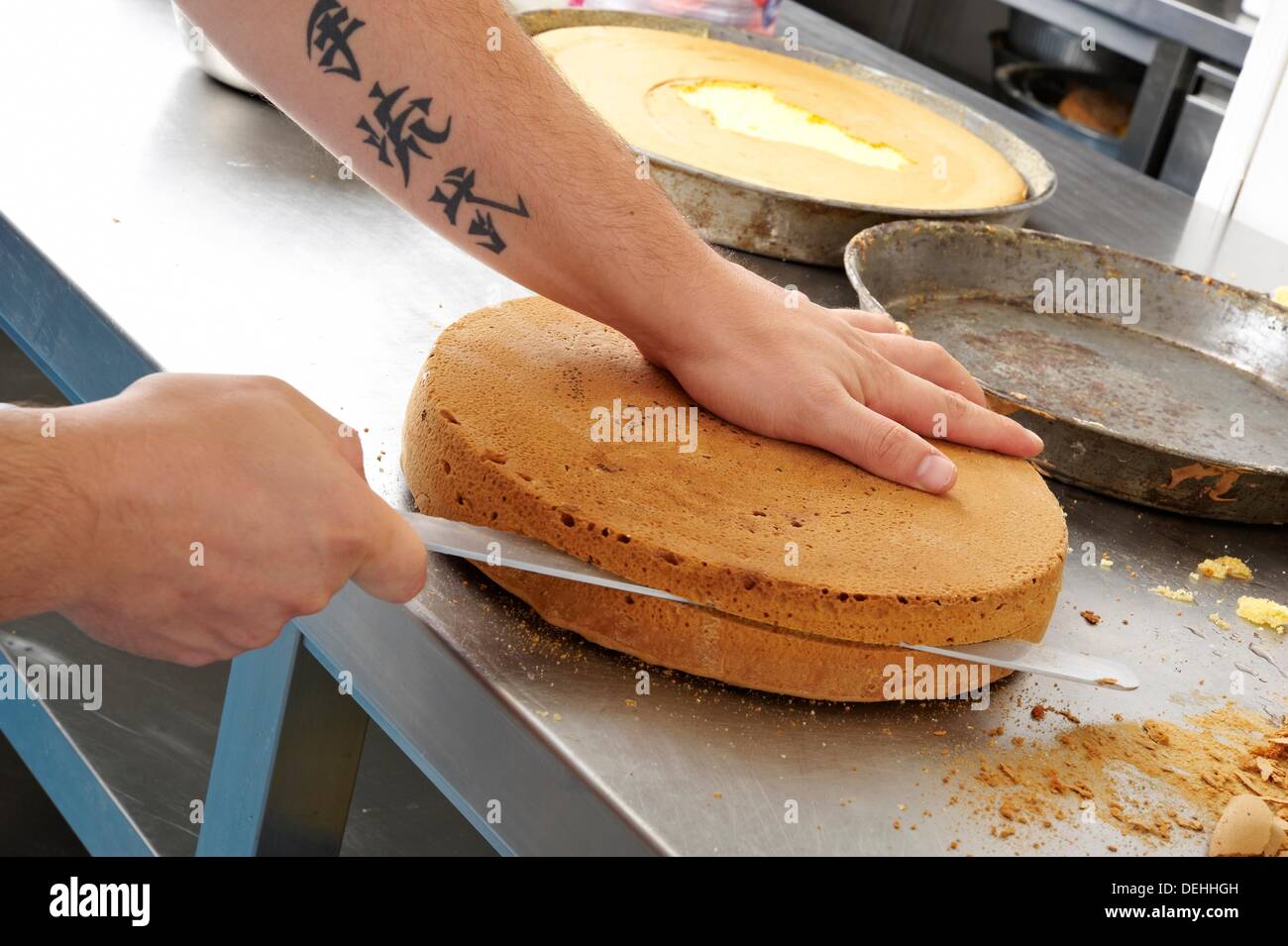 A pastry chef cutting in two a sponge cake using a kitchen knife Stock