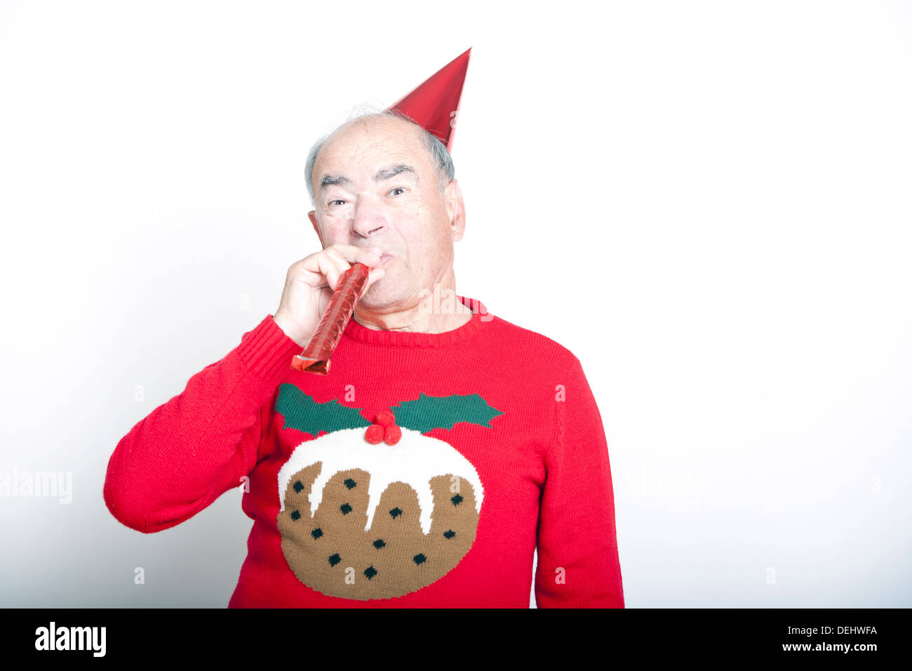 Senior adult man wearing Christmas jumper blowing party blower Stock Photo