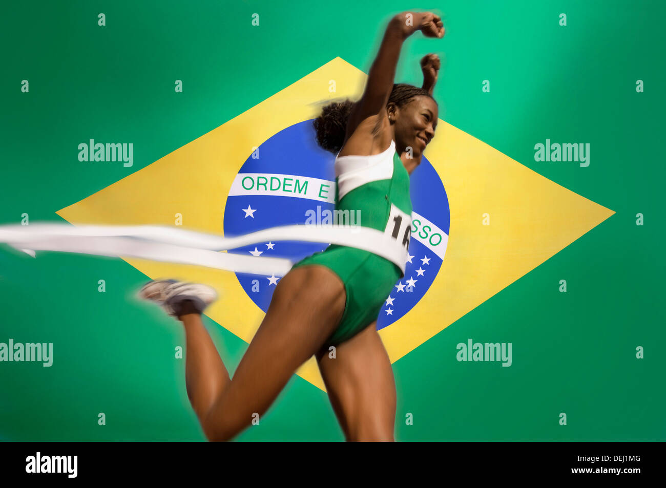 Runner Breaking through the finishing line tape over Brazilian flag Stock Photo