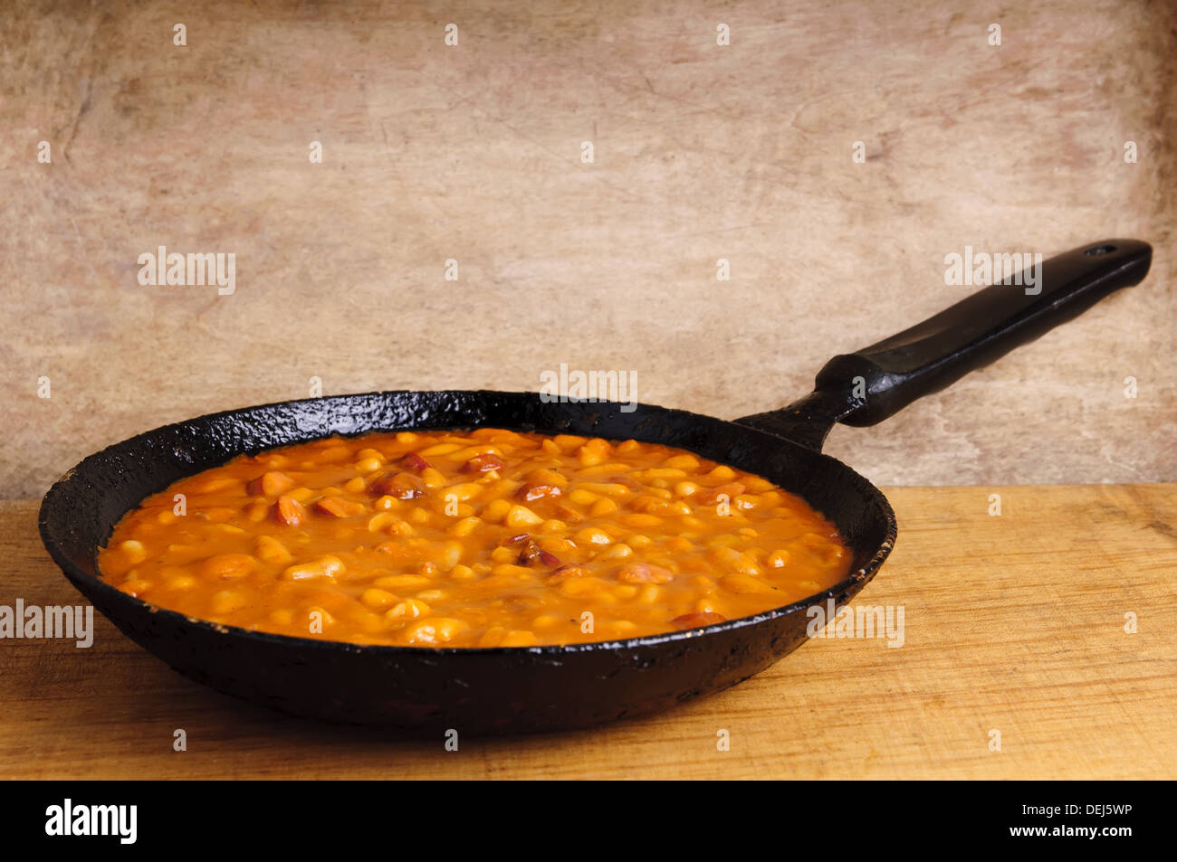 traditional homemade meal with beans and sausages in a pan on a wooden background Stock Photo