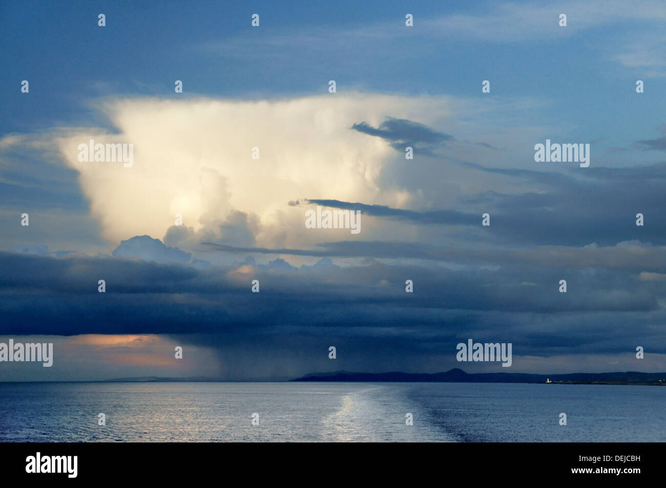 Anvil top cumulonimbus rain cloud rises above stratocumulus and rain shower over Corsewall Lighthouse, Loch Ryan, Irish Sea, UK Stock Photo