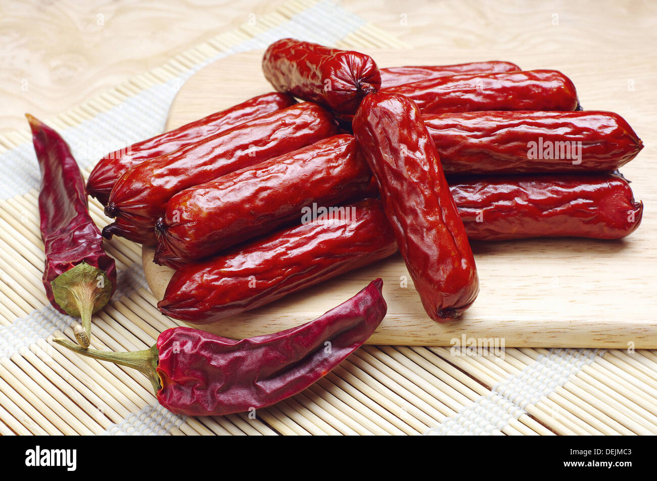Small smoked sausages and dry chili peppers on a cutting board Stock Photo