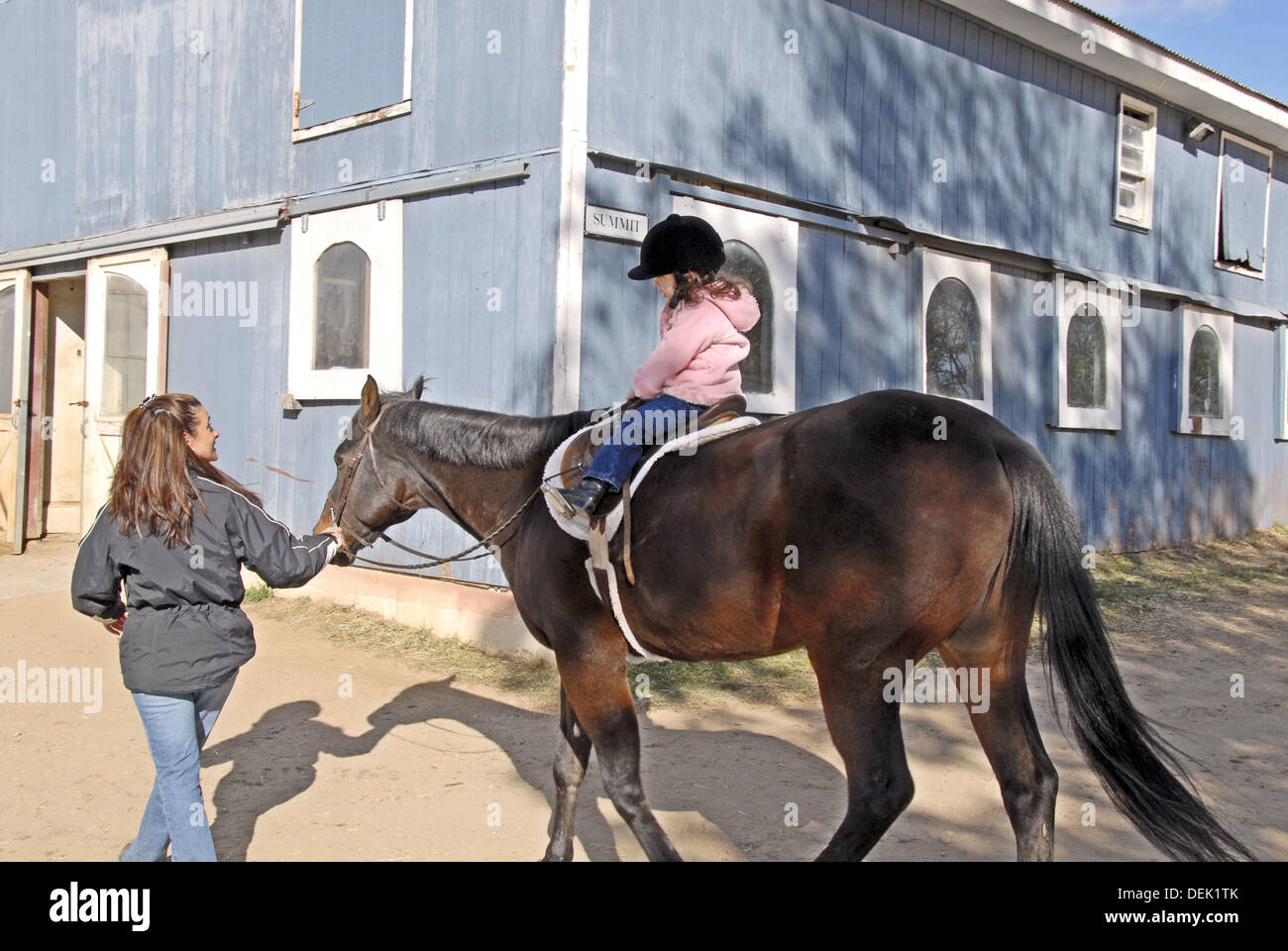 Three year old girl riding a horse; mother leading, at Stanhope Stables