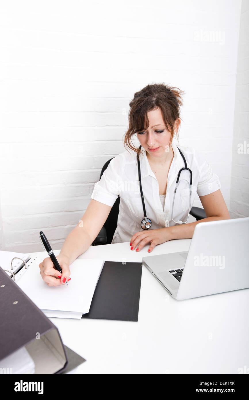 Young female doctor writing notes on desk clinic Stock Photo