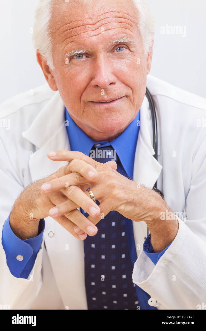 A senior man male medical hospital doctor sitting at a desk wearing a