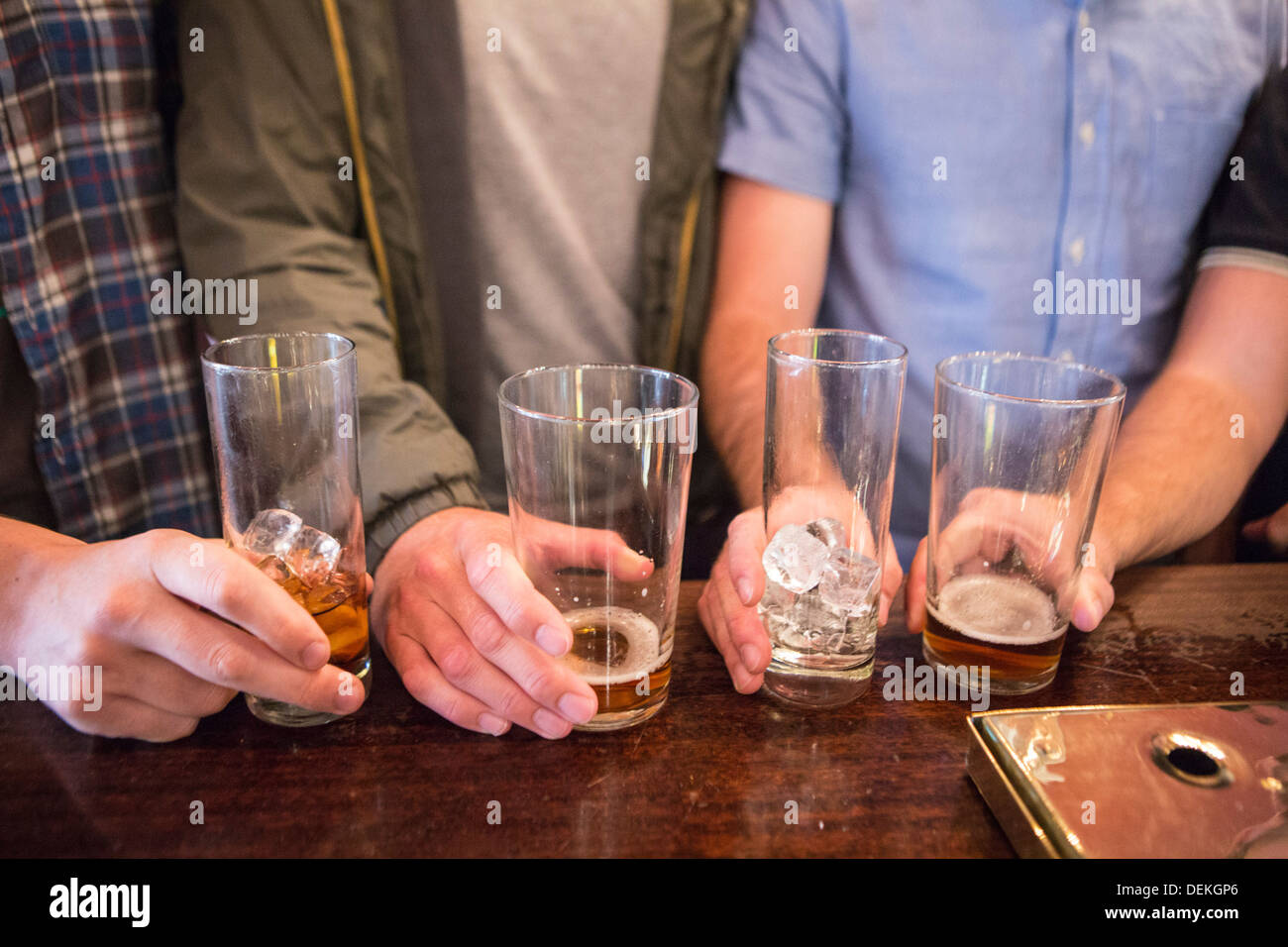 Four white British men line up their pint glasses on a bar in an English pub in London, United Kingdom. Stock Photo