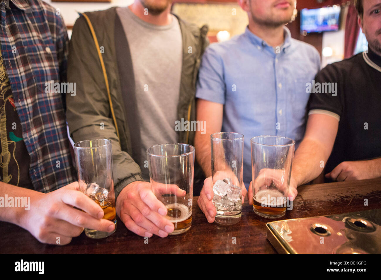 Four white British men line up their pint glasses on a bar in an English pub in London, United Kingdom. Stock Photo