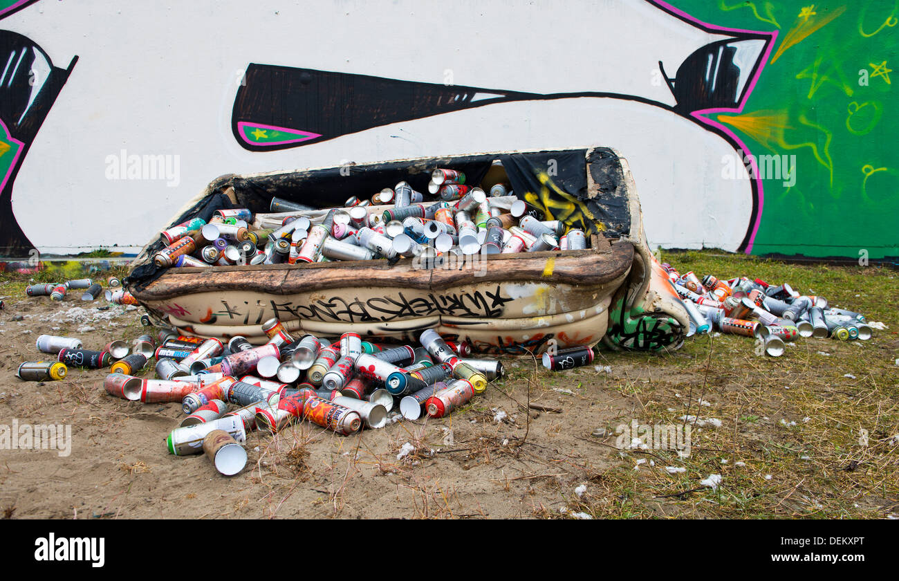 Dumpster filled with spray paint cans on city street with graffiti Stock Photo