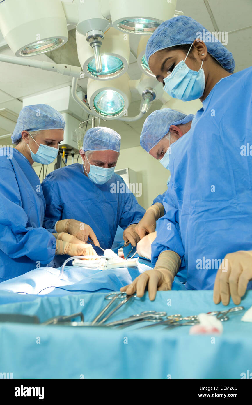 Interracial team medical doctors male female surgeons in surgery operating on patient using in theater wearing scrubs & masks Stock Photo