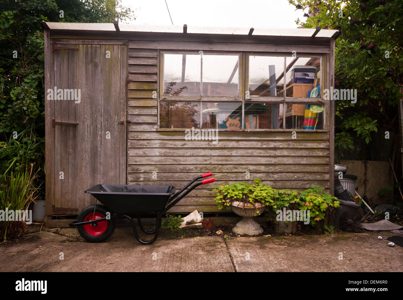 Exterior Of A Wooden Garden Shed With An Empty Metal Wheelbarrow Outside Stock Photo