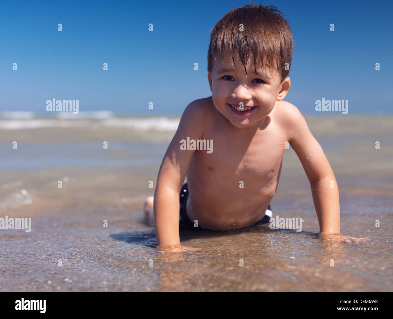 Portrait of a happy smiling three year old boy lying on a sandy shore in the water Stock Photo