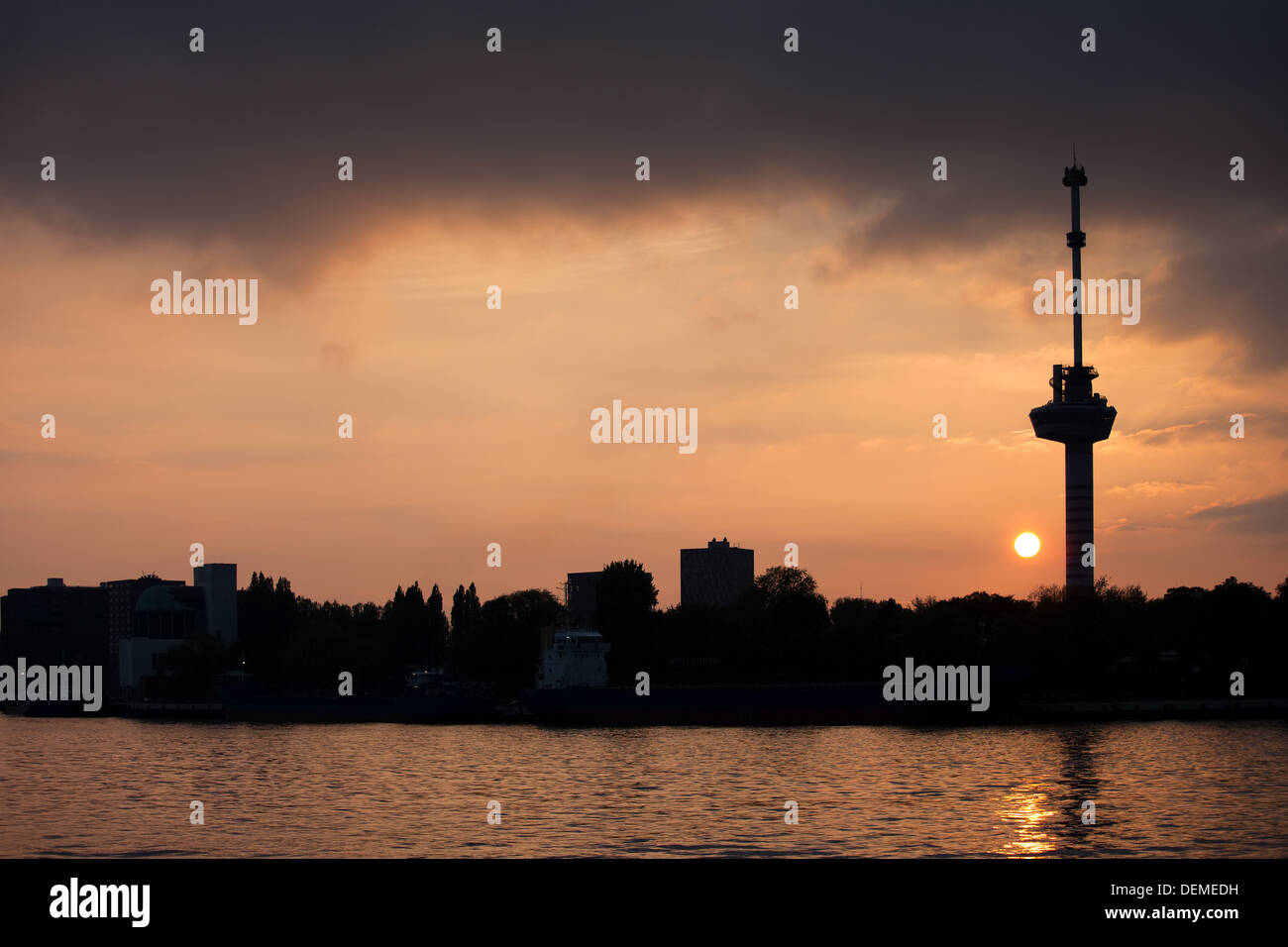 A panoramic view of the Rotterdam city skyline at sunset, as seen from the Euromast observation tower, with illuminated buildings and the Maas River winding through.