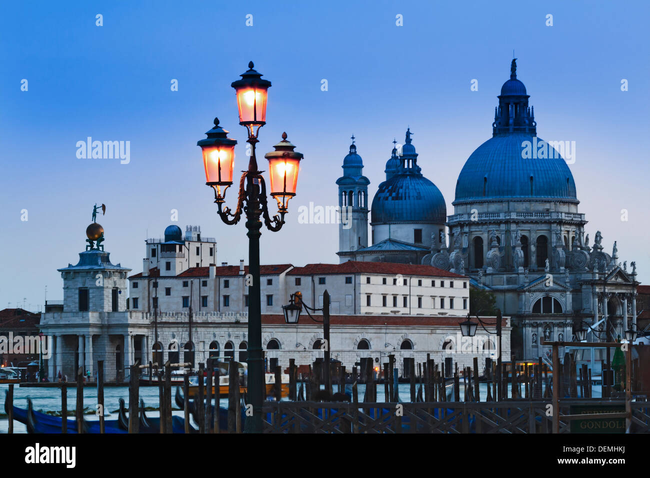 Italy Venice island city at sunset view over gandola poles to Santa Maria della salute cathedral over canal illuminated murano g Stock Photo
