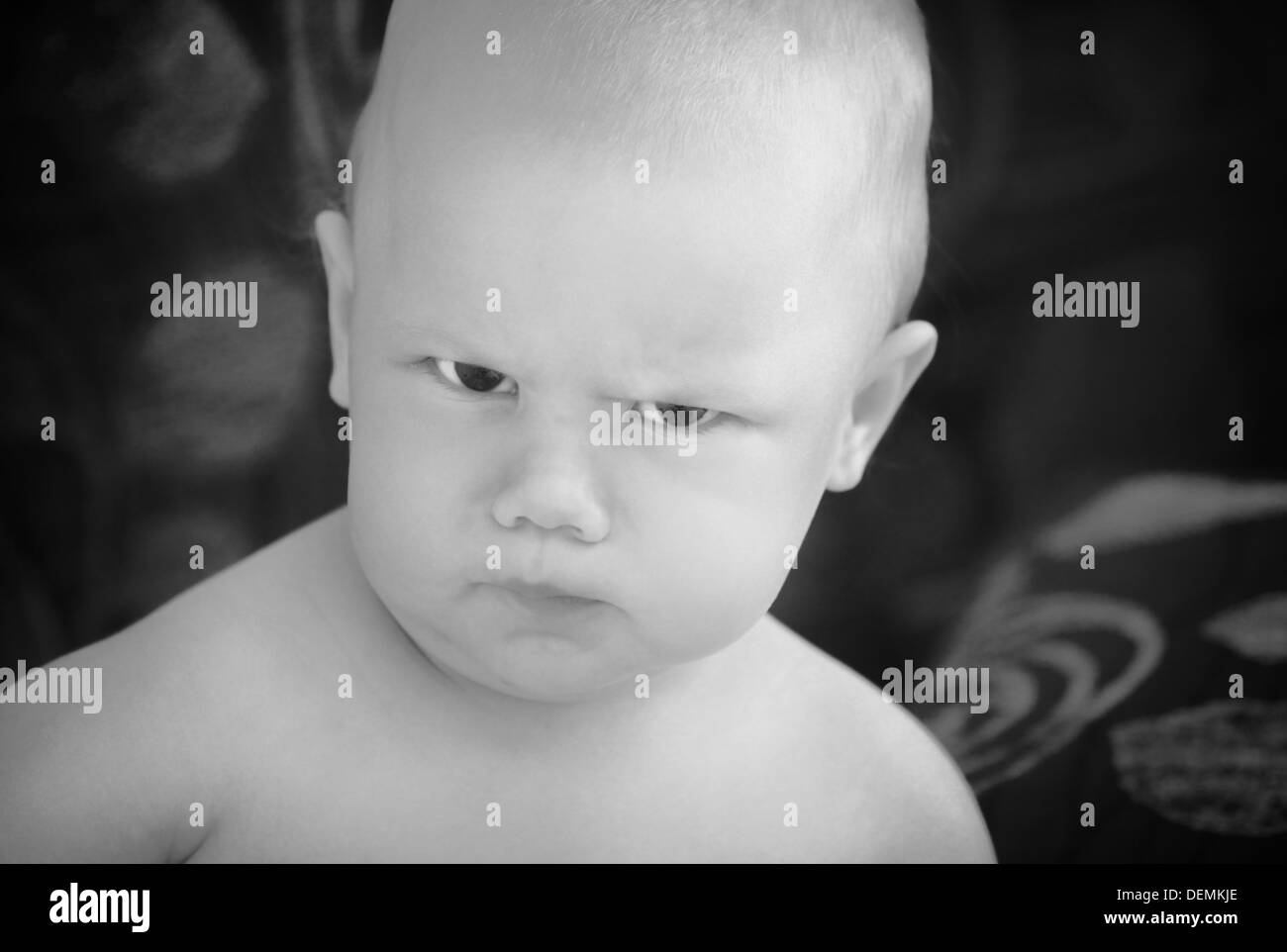 Funny angry baby girl close-up monochrome portrait on dark blurred background Stock Photo