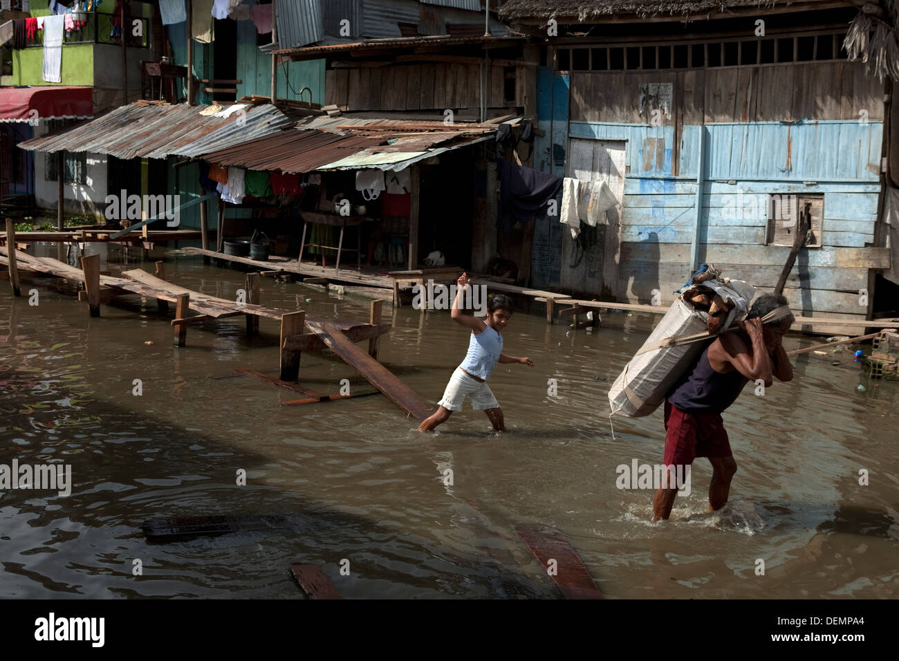 A man walks loaded together with her daughter through the flooded streets by the swelling of Amazon River. Iquitos. Stock Photo