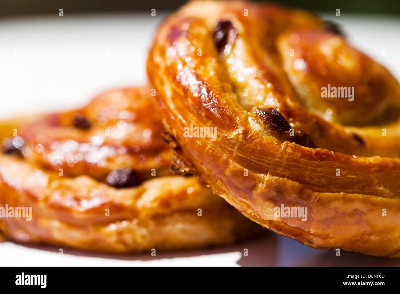 Two mouth watering flaky sultana danish pastry's on a plate, outdoors,  on a table in the sun Stock Photo