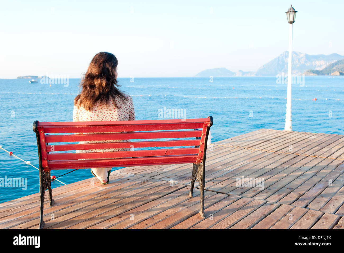 girl sitting on a bench on the pier at the sea and reflects Stock Photo ...
