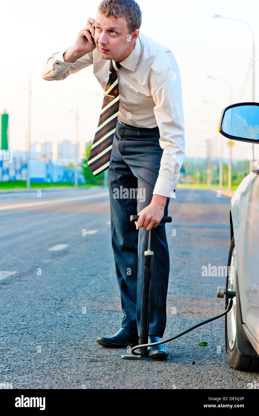 businessman pumps the pump wheel of a car and talking on the phone