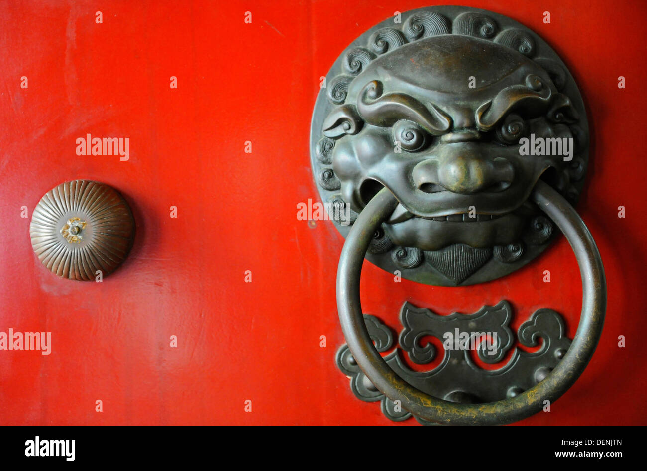 An ornate door knocker in the shape of a fierce warrior on the front of a studded red door. Stock Photo