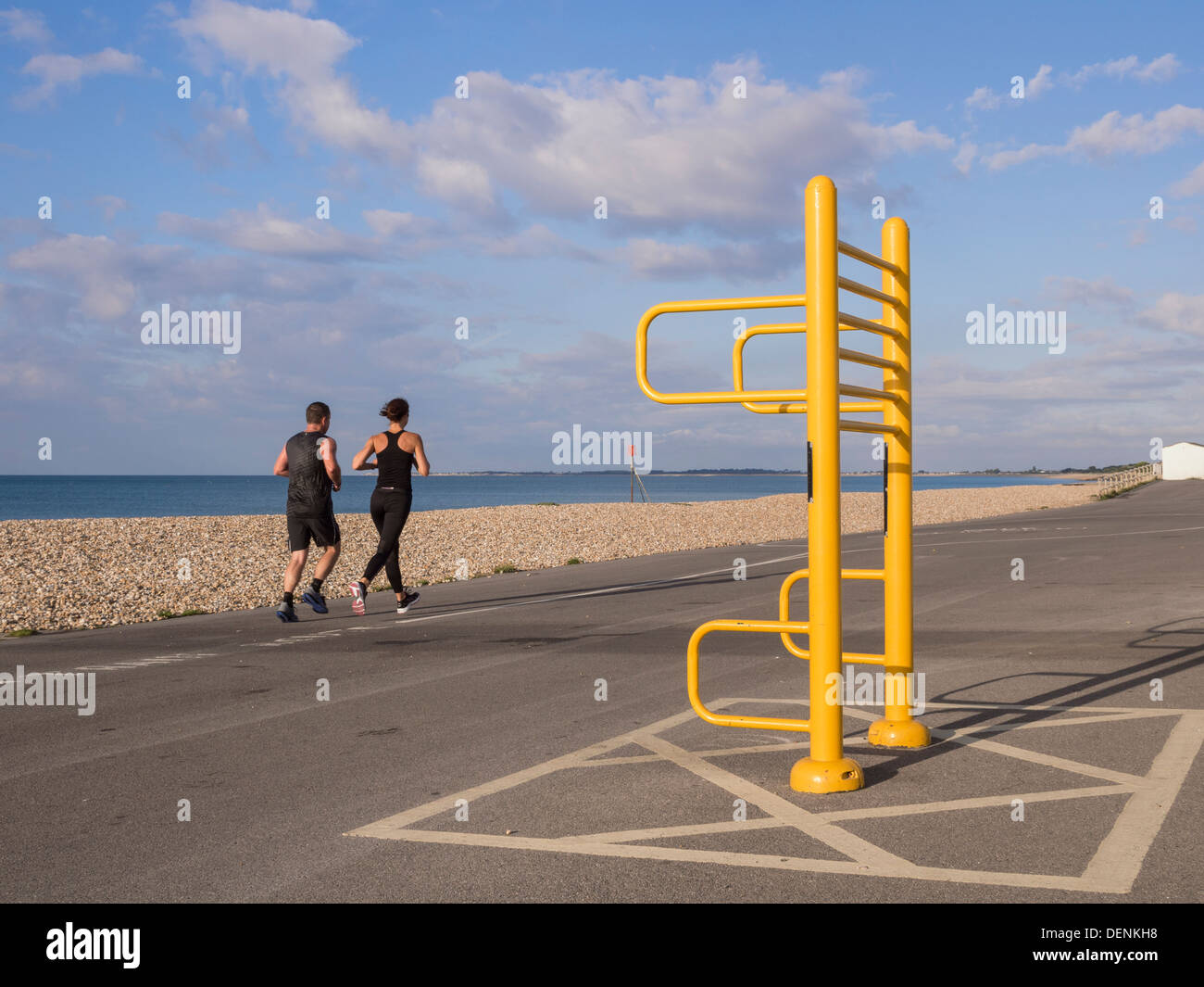 Two people jogging along sea front promenade with trim trail apparatus in Aldwick Bognor Regis West Sussex England UK Britain Stock Photo