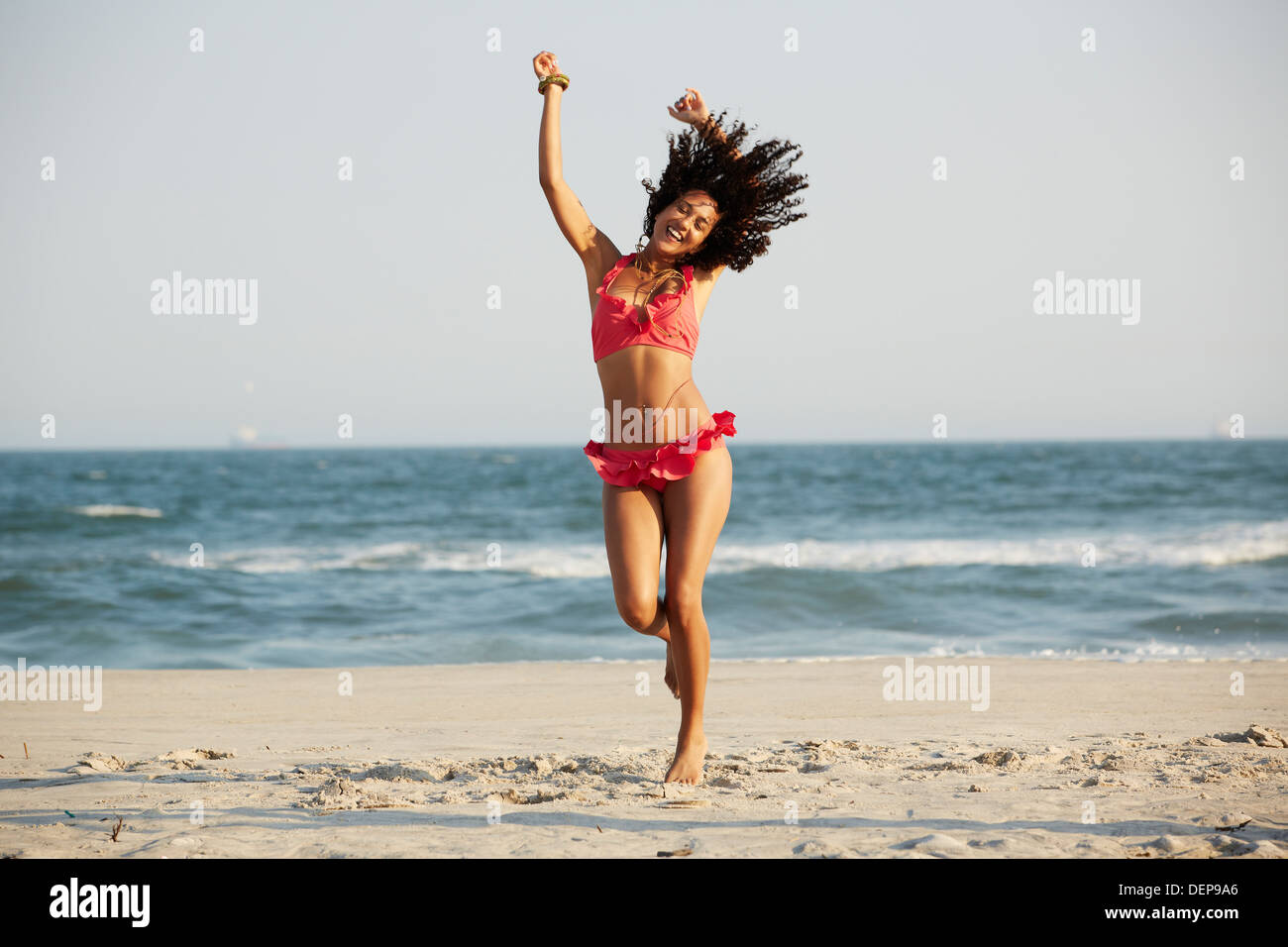 Mixed race woman jumping for joy on beach Stock Photo