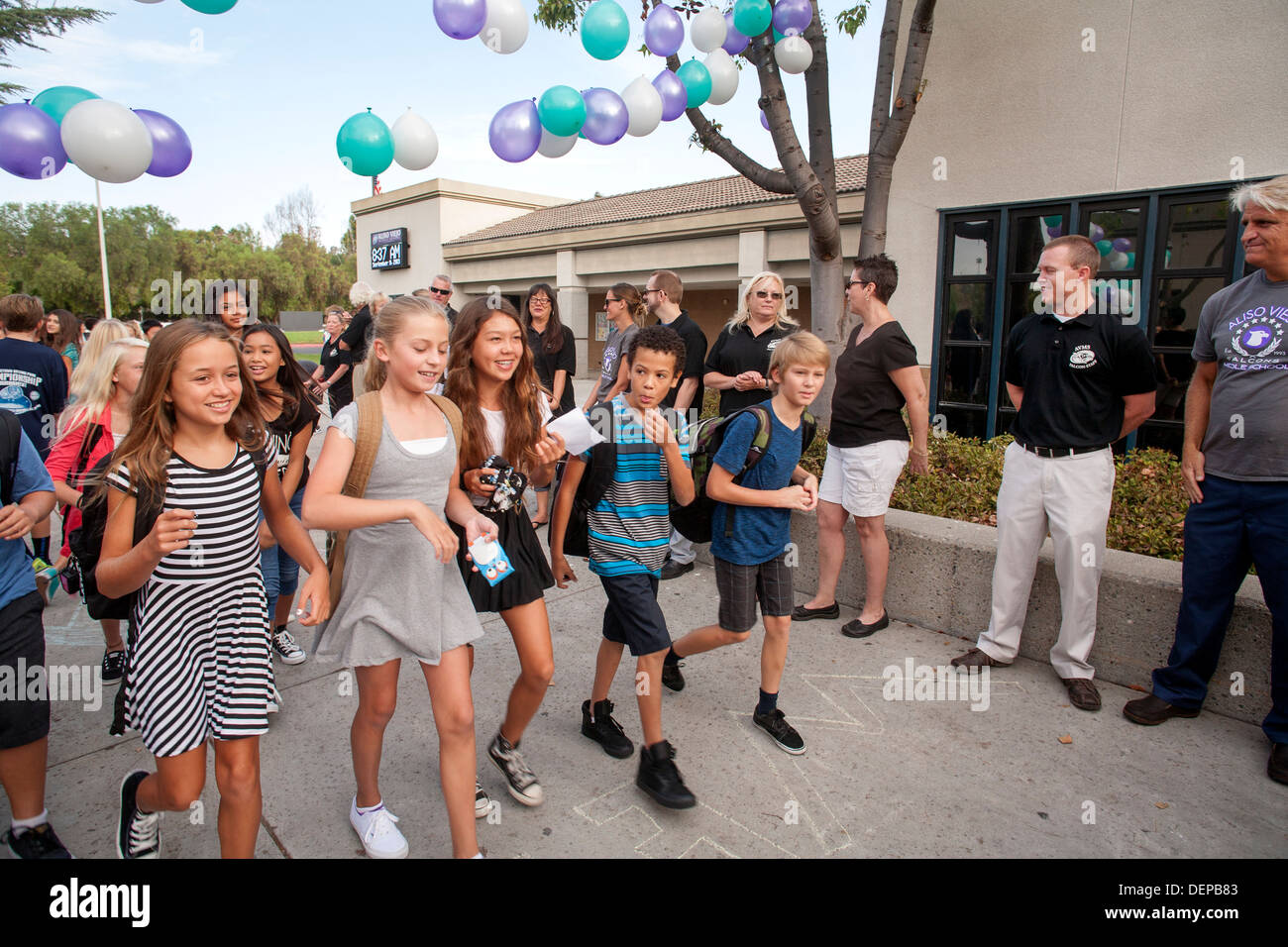 Multiethnic middle school girls greet each other on the first day of school in Aliso Viejo, CA. Note teachers in background Stock Photo