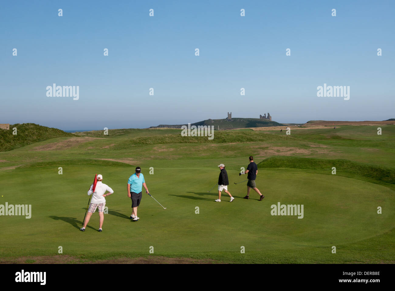 Golfers on a course next to the ruins of Dunstaborough Caslte, Embleton, Northumberland Stock Photo