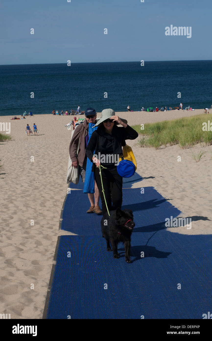 Tourists leave Race Point Beach in Provincetown, MA after a day in the sun with their dog. Note blue mat used to prevent erosion Stock Photo