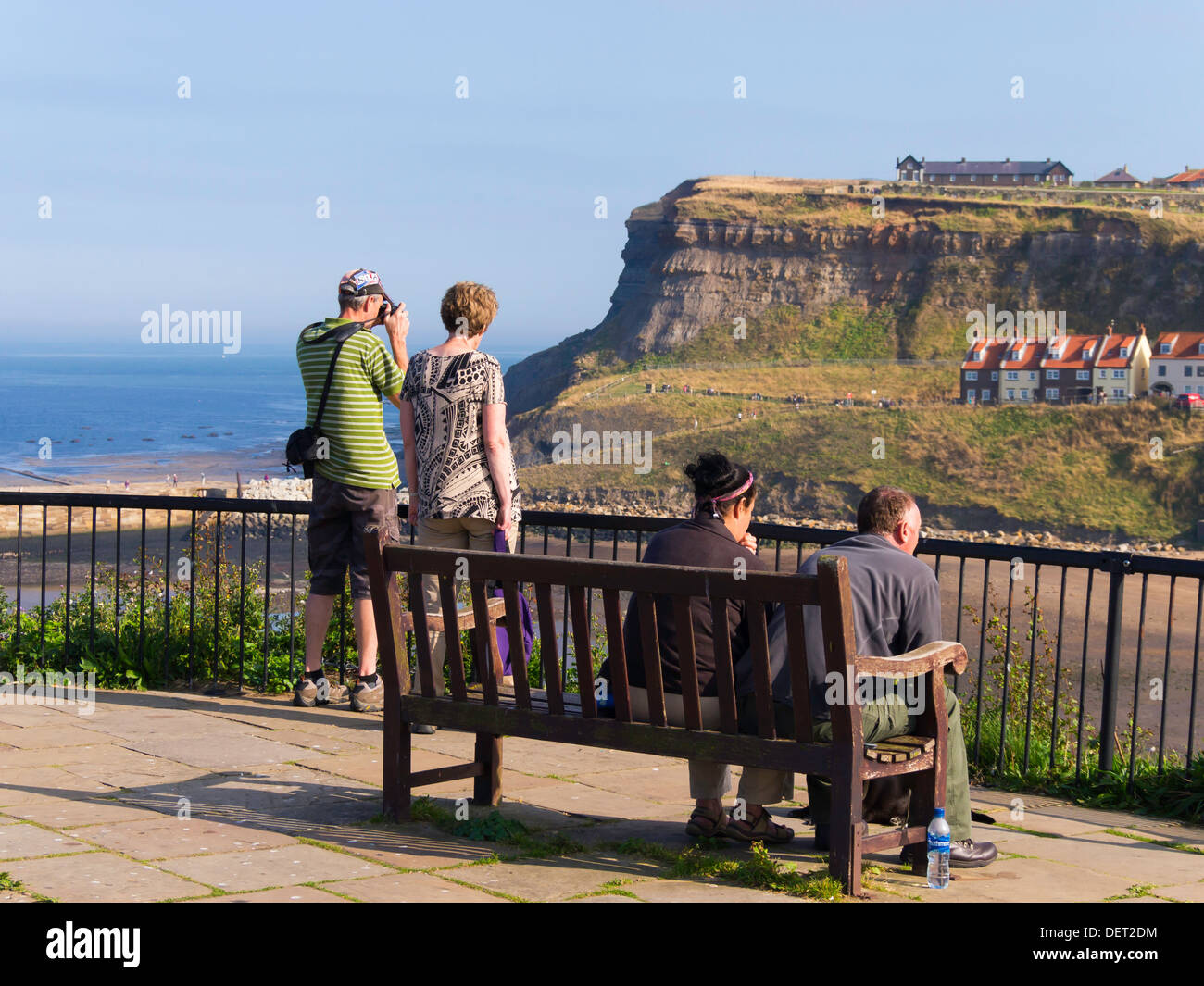 Sightseers on a late summer day enjoy the view from a vantage point on Whitby west cliff looking over the harbour to east cliff Stock Photo