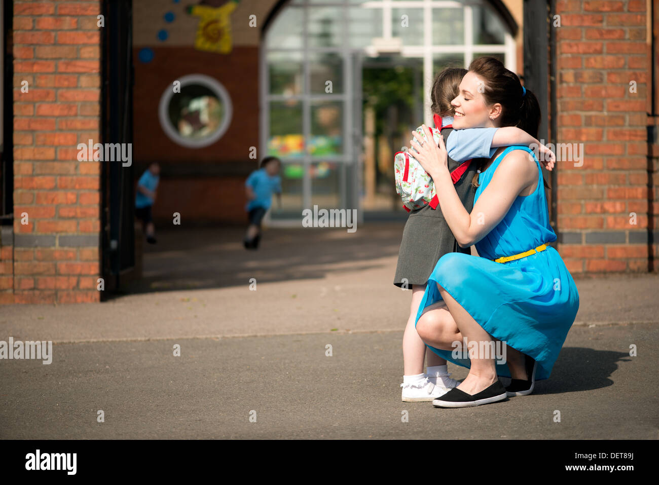 An attractive happy young mum comforting & picking up or dropping off her daughter at the infant school gates Stock Photo