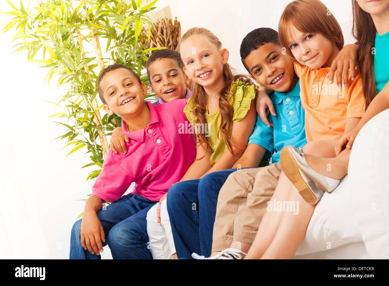 Close portrait of group of diversity looking kids sitting on the couch at home, hugging, smiling and laughing  Stock Photo