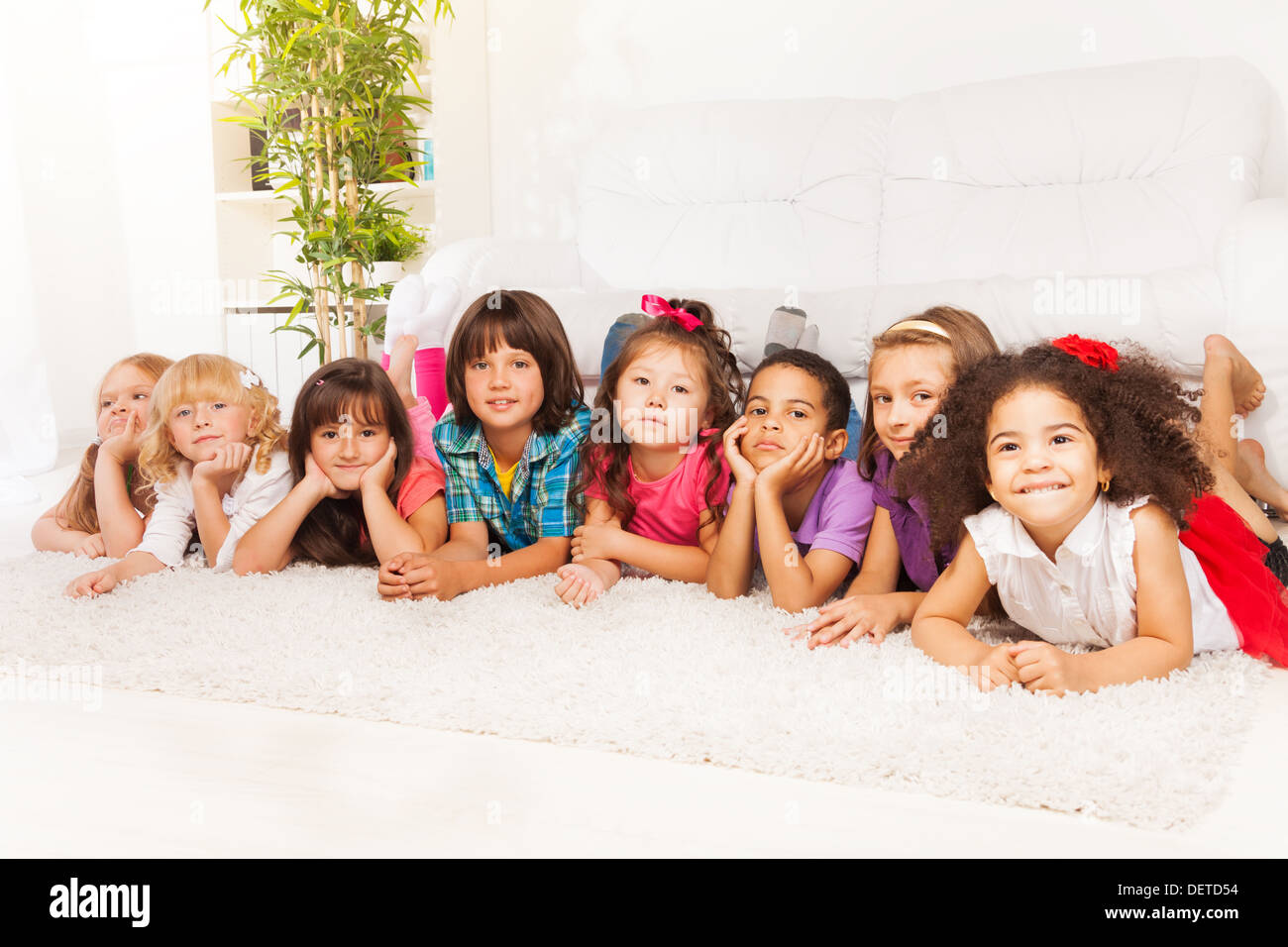 Group of eight little kids, boys and girls, black, Asian and Caucasian laying on the floor at home in living room looking at camera Stock Photo