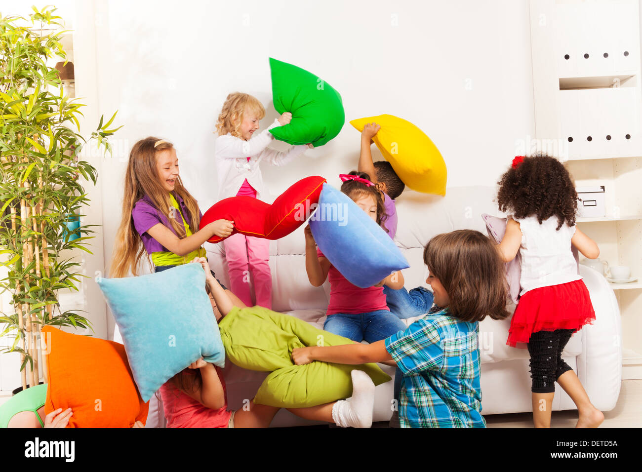 Pillow fight - large group of kids actively playing with pillow in the living room on the coach Stock Photo