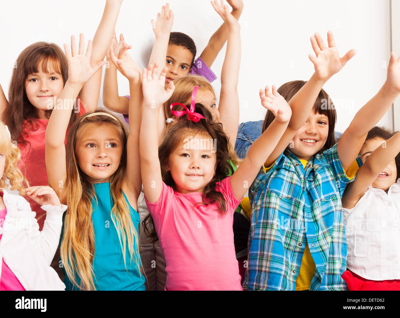 Closeup portrait group of seven happy little 5-6 years old kids, boys and girls, black, Asian and Caucasian sitting on the coach with with lifted hands and happy faces Stock Photo