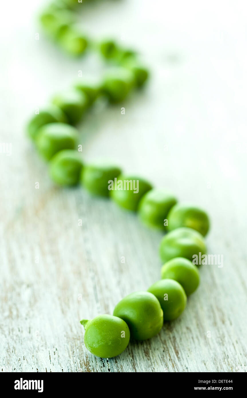 Fresh green peas lined up in a wavy line on a rustic white wood surface. Stock Photo