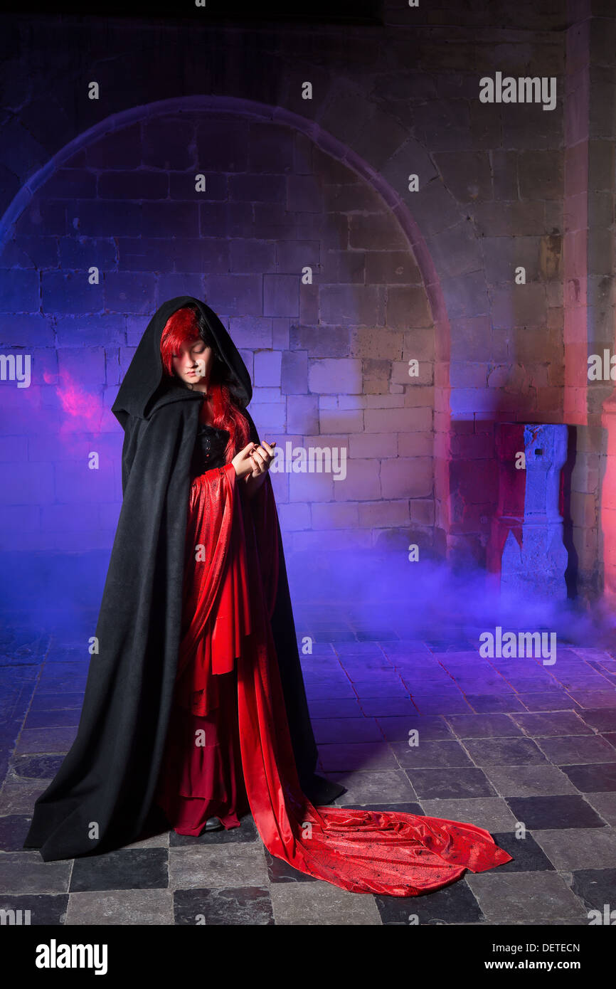 Beautiful gothic victorian woman in red standing in a smokey dark medieval castle Stock Photo