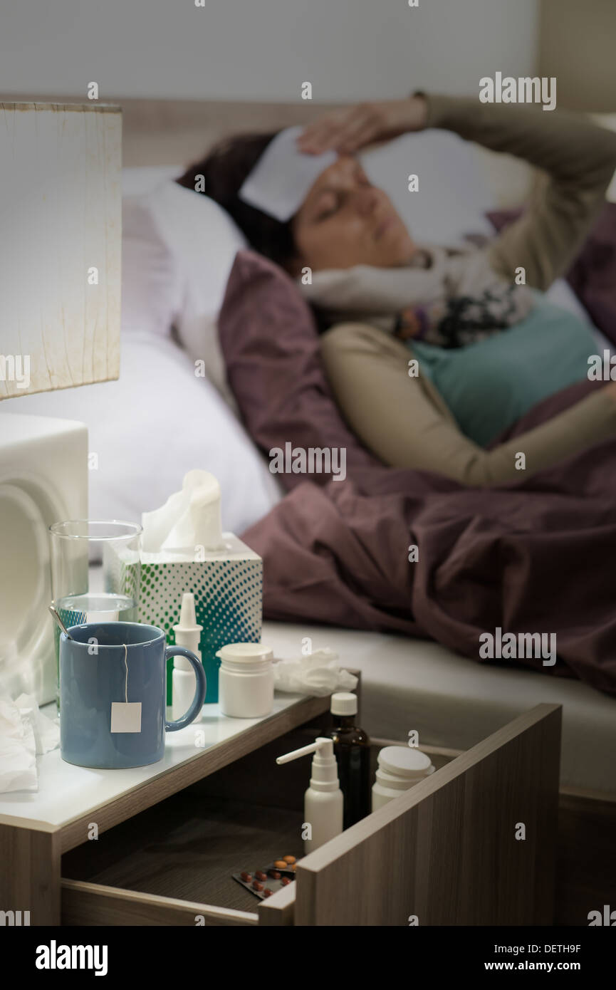 Flu medicines on bedside table beside ill woman in bed Stock Photo
