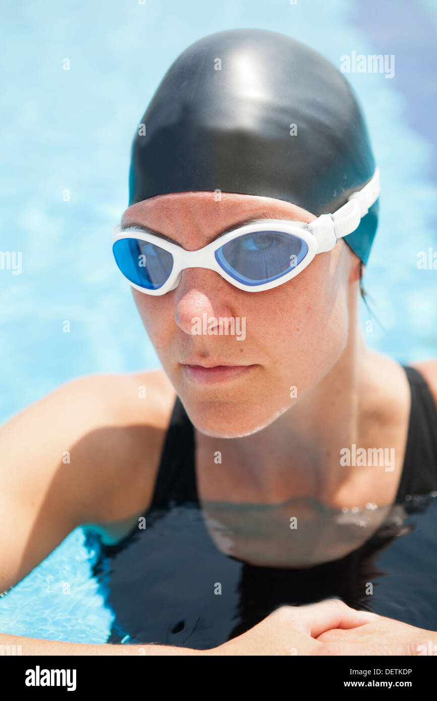 Female swimmer resting at edge swimming pool concetrating and peering through goggles Stock Photo