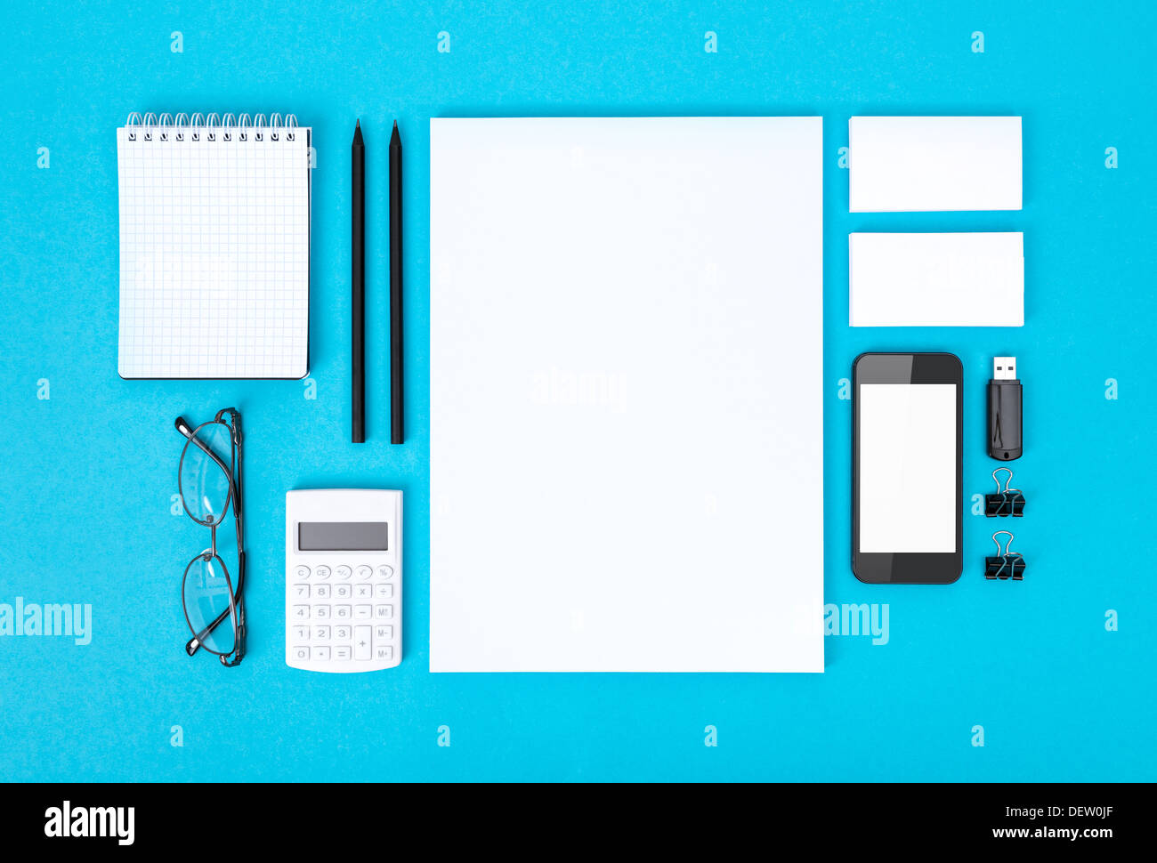 Set of variety blank office objects organized for company presentation or corporate identity. Isolated on blue paper background. Stock Photo