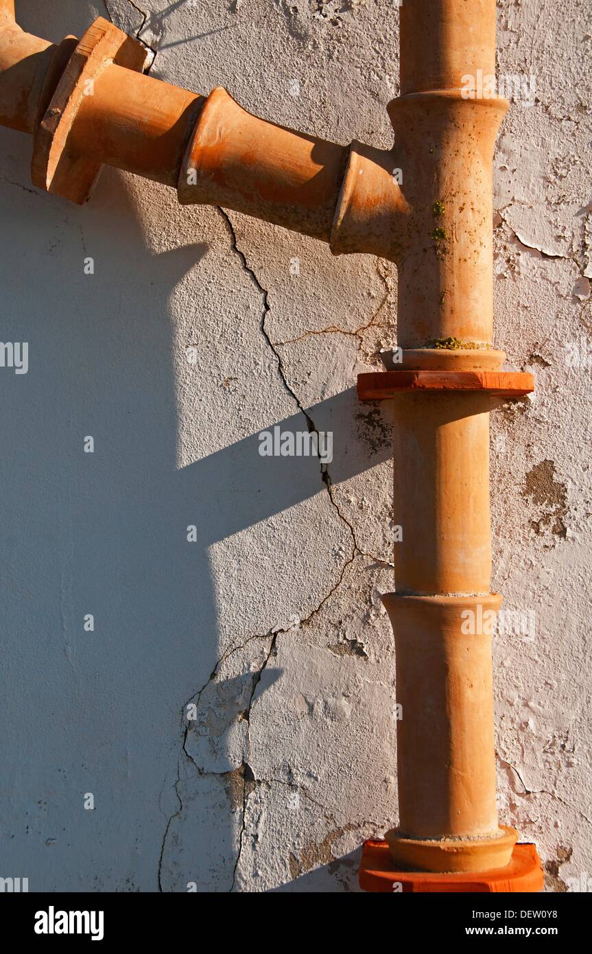 Stoneware sewage pipe against a stone, cracked wall Stock Photo