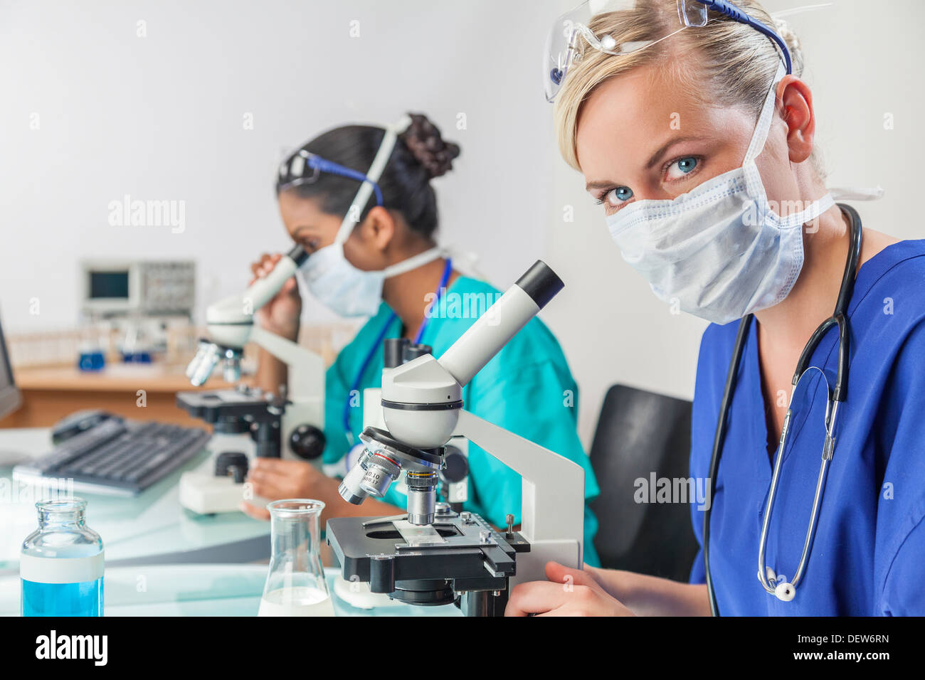 Blond female medical scientific researcher or doctor using microscope in laboratory with an Indian Asian colleague beside her Stock Photo